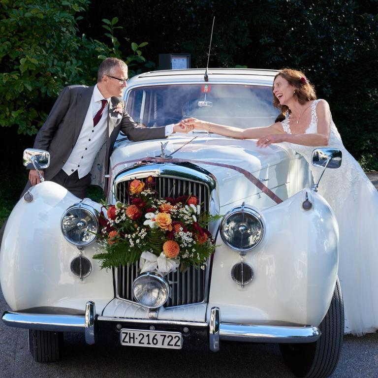 Hochzeitspaar bei Auto stehend schauen sich an